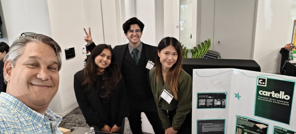 Ochi and the three students stand next to a poster about Cartello